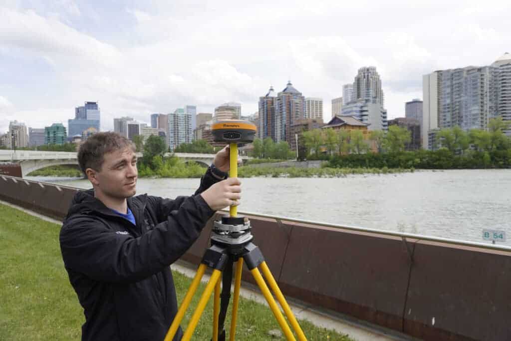 Man setting up GNSS equipment in front of river and downtown