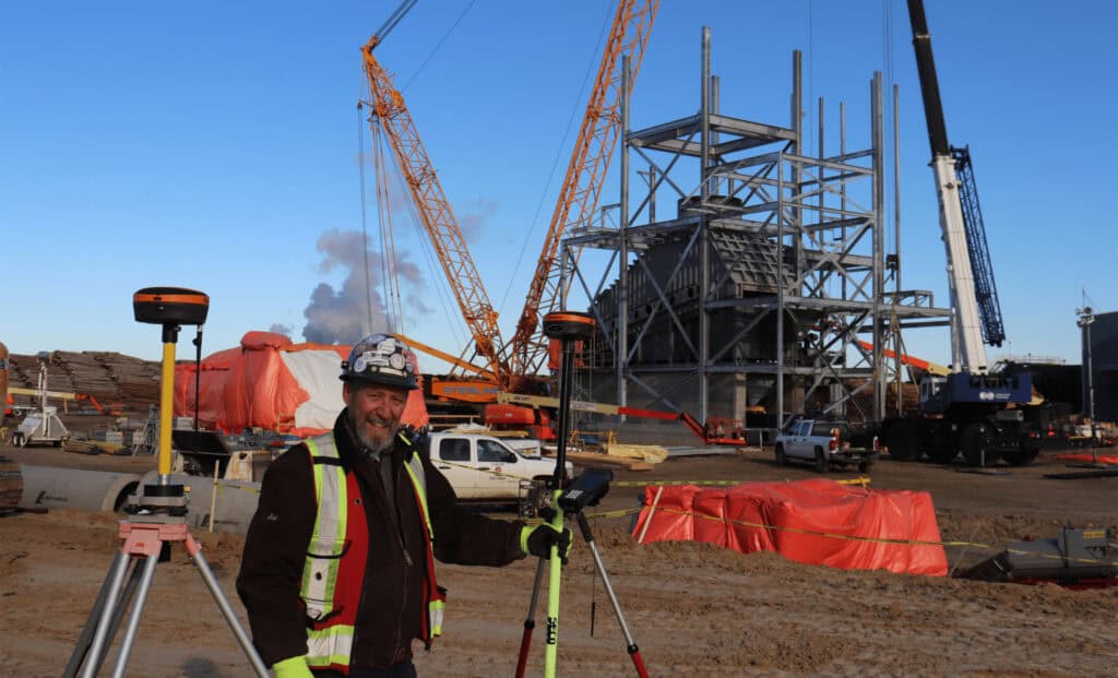 Surveyor using RTK base station at construction site with cranes and steel structure