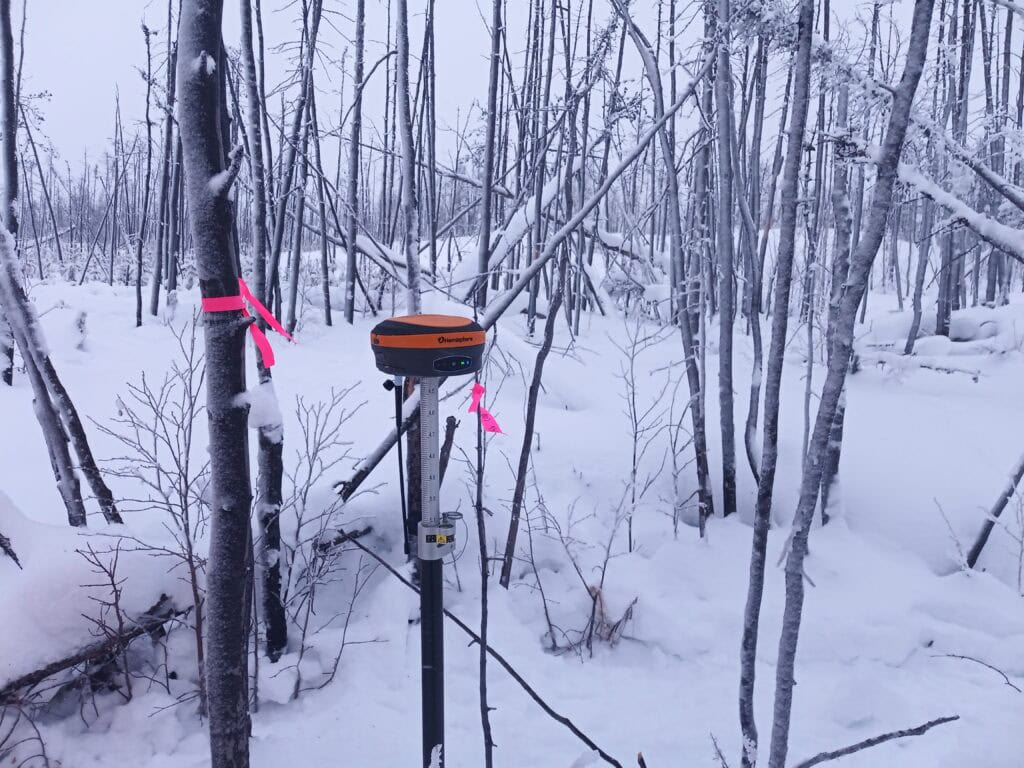 GNSS receiver set up in a snowy forest during winter surveying conditions