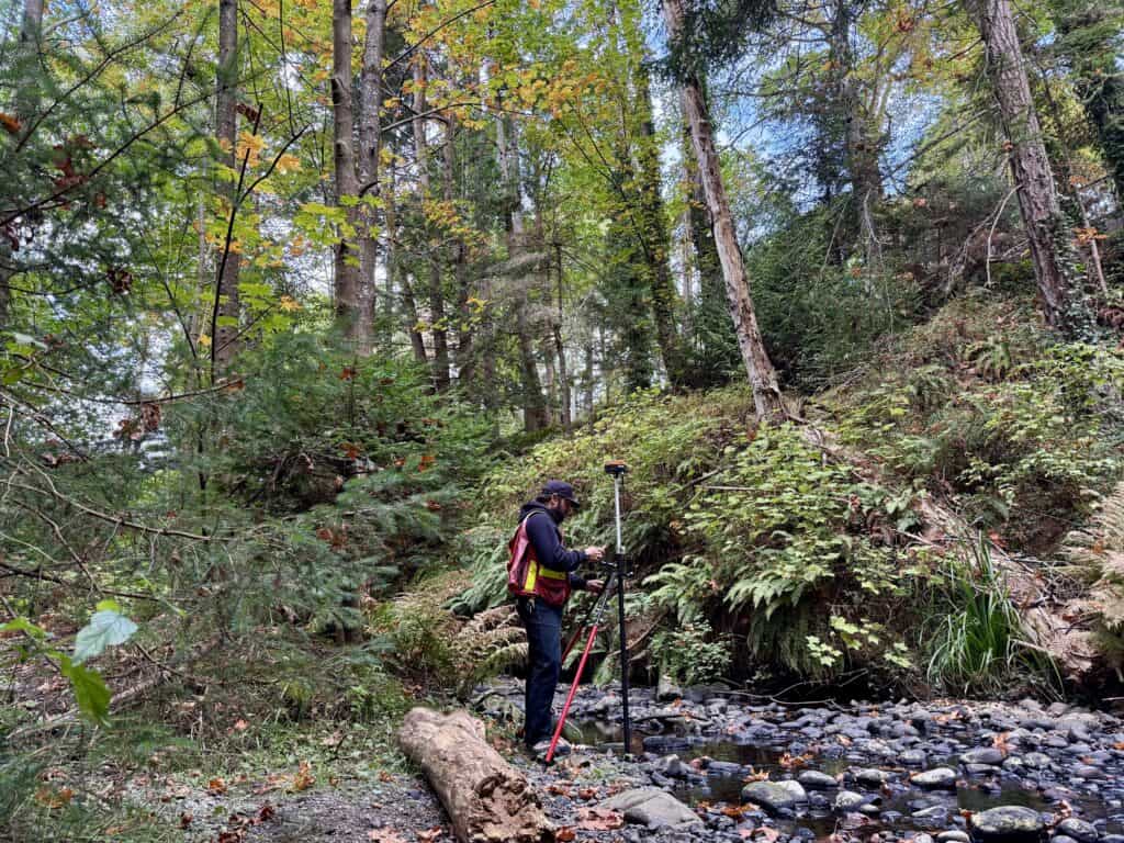 Surveyor using RTK GNSS receiver on tripod for high-accuracy positioning in forested terrain