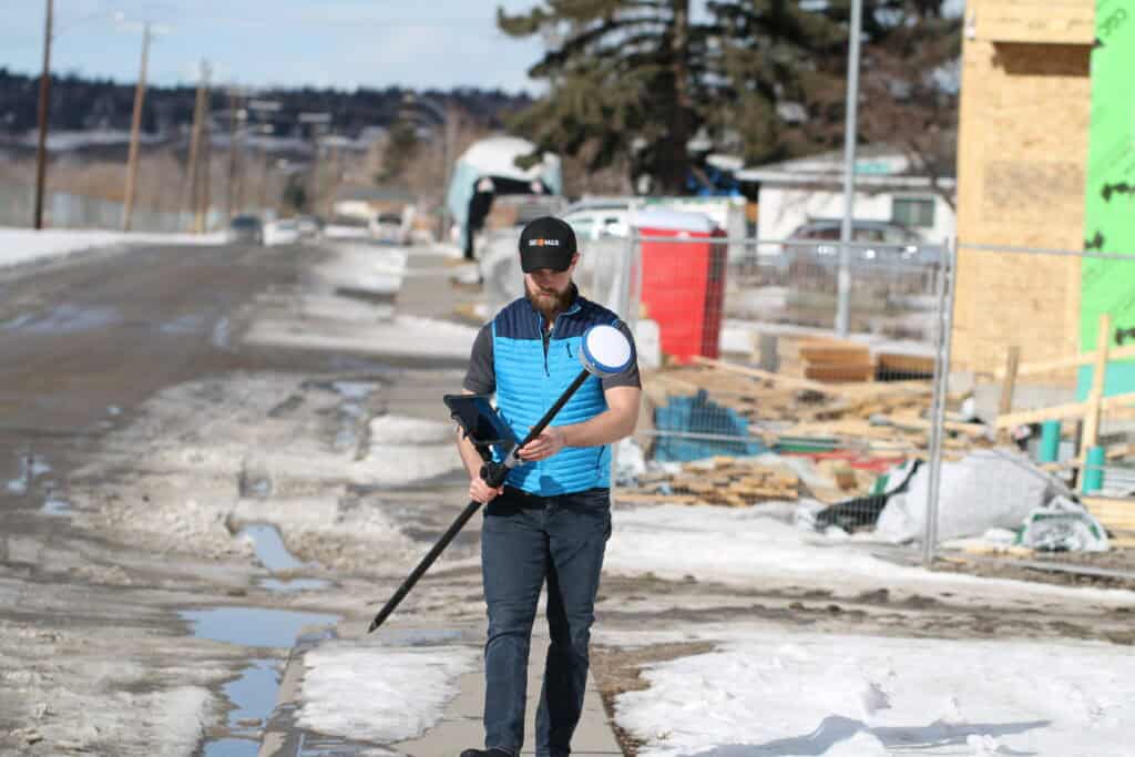 Surveyor using GNSS rover collecting road construction survey data on job site