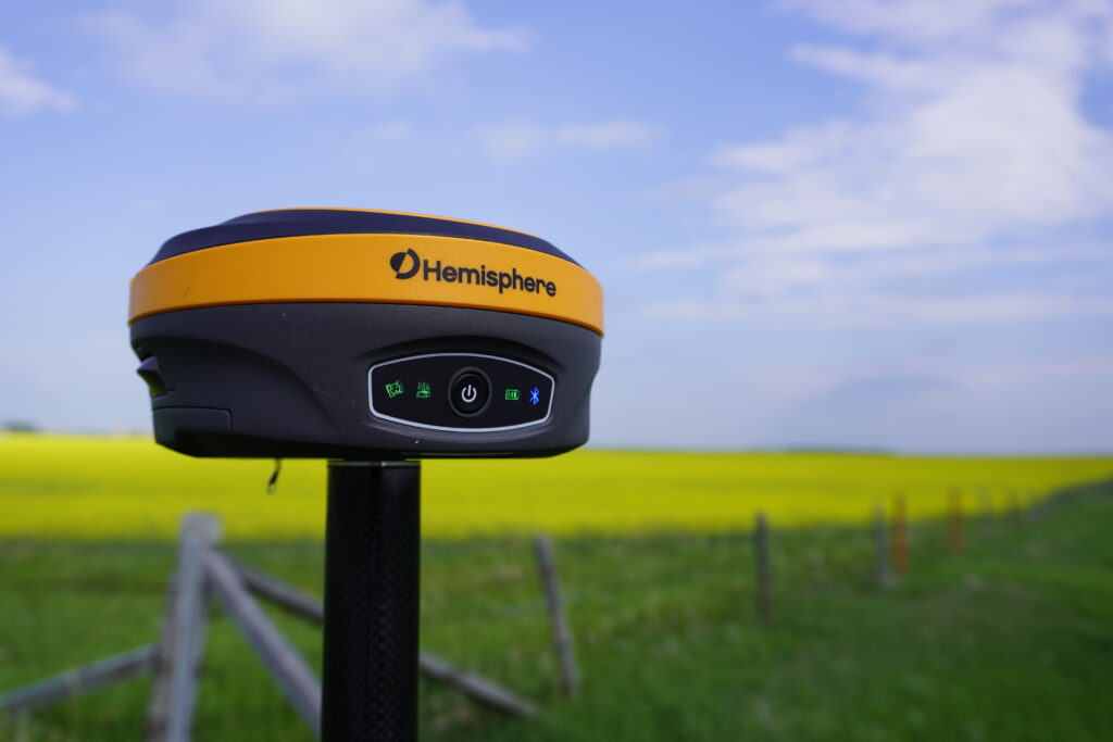 Hemisphere GNSS RTK receiver on a survey pole in an open canola field under clear sky