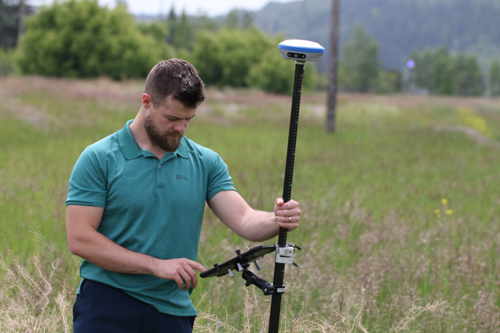 Surveyor entering data on a rugged data collector mounted to an RTK GNSS rover pole in a grassy field